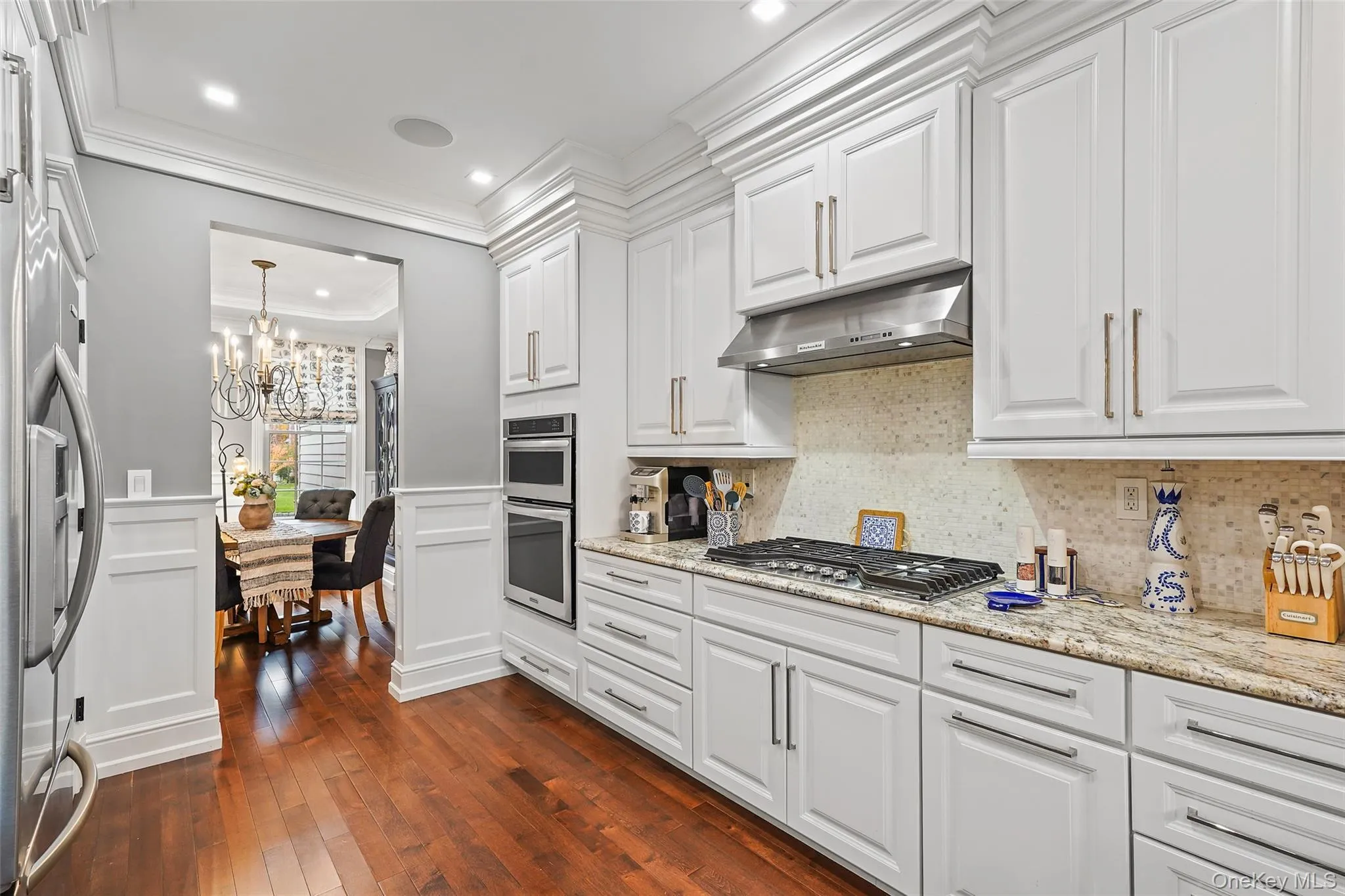Kitchen featuring white cabinets, light stone counters, dark wood finished floors, crown molding, and stainless steel appliances Kitchen featuring white cabinets, light stone counters, dark wood finished floors, crown molding, and stainless steel appliances