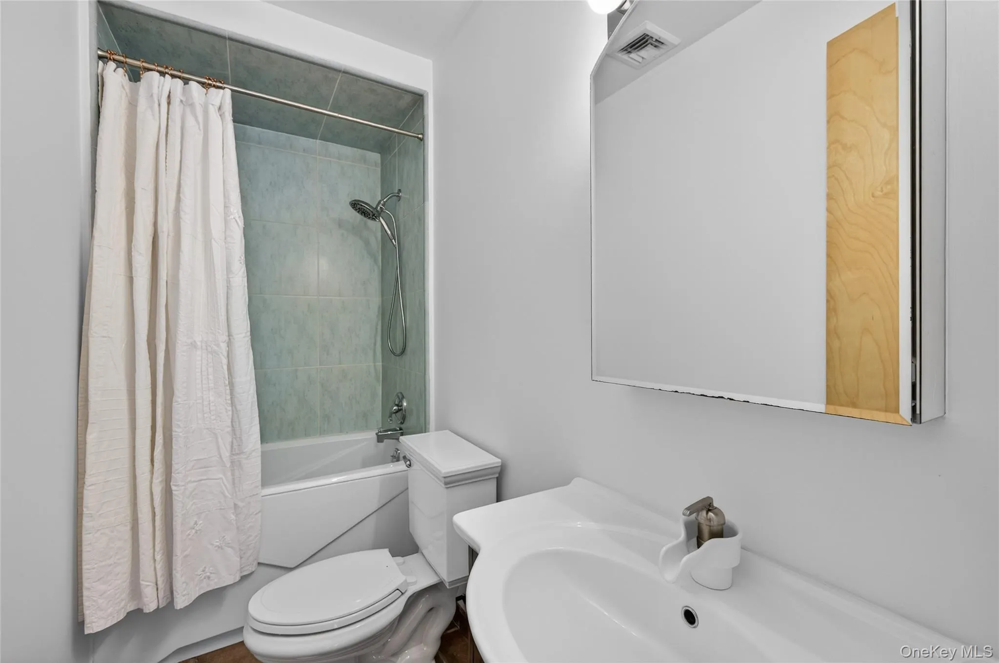 Bathroom featuring a white vanity with integrated sink, large mirrored medicine cabinet, and a shower-over-tub combination with light-toned wall tiling Bathroom featuring a white vanity with integrated sink, large mirrored medicine cabinet, and a shower-over-tub combination with light-toned wall tiling