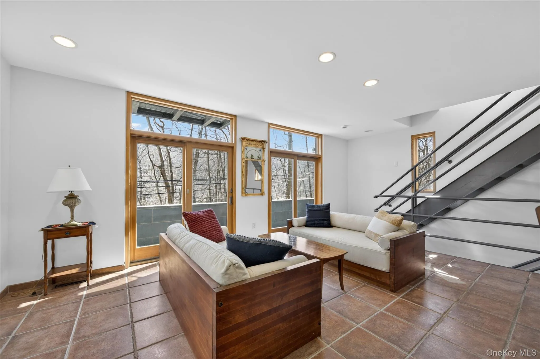 Living area featuring large format terracotta-style tile flooring, recessed ceiling lighting, and a contemporary open-riser staircase with metal railings Living area featuring large format terracotta-style tile flooring, recessed ceiling lighting, and a contemporary open-riser staircase with metal railings