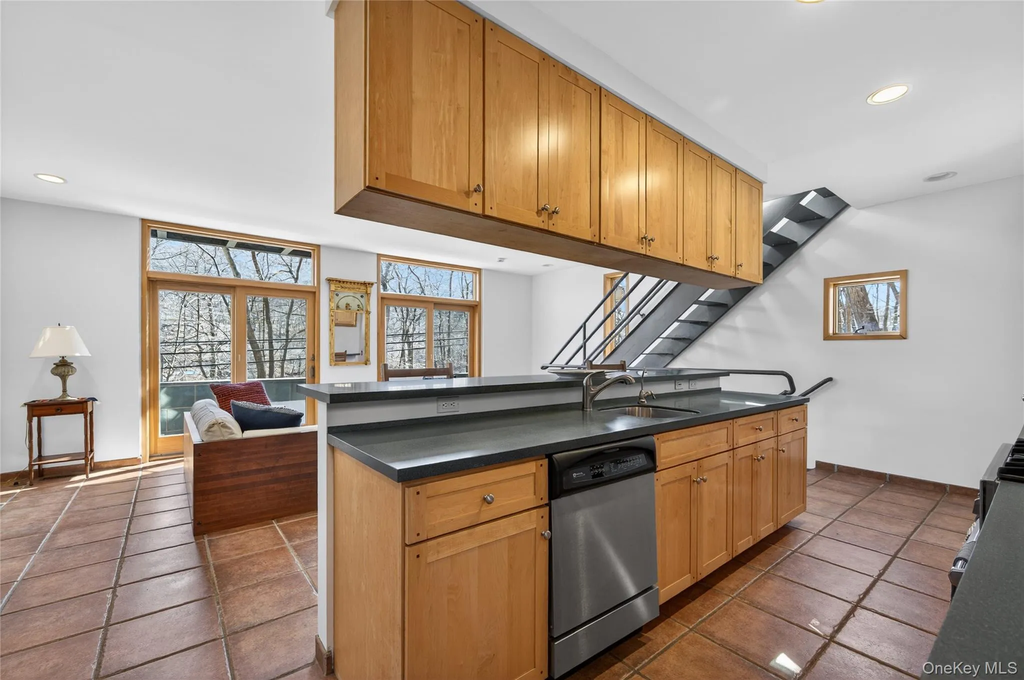 Kitchen featuring wood cabinetry, stainless steel dishwasher, and a contemporary metal staircase Kitchen featuring wood cabinetry, stainless steel dishwasher, and a contemporary metal staircase