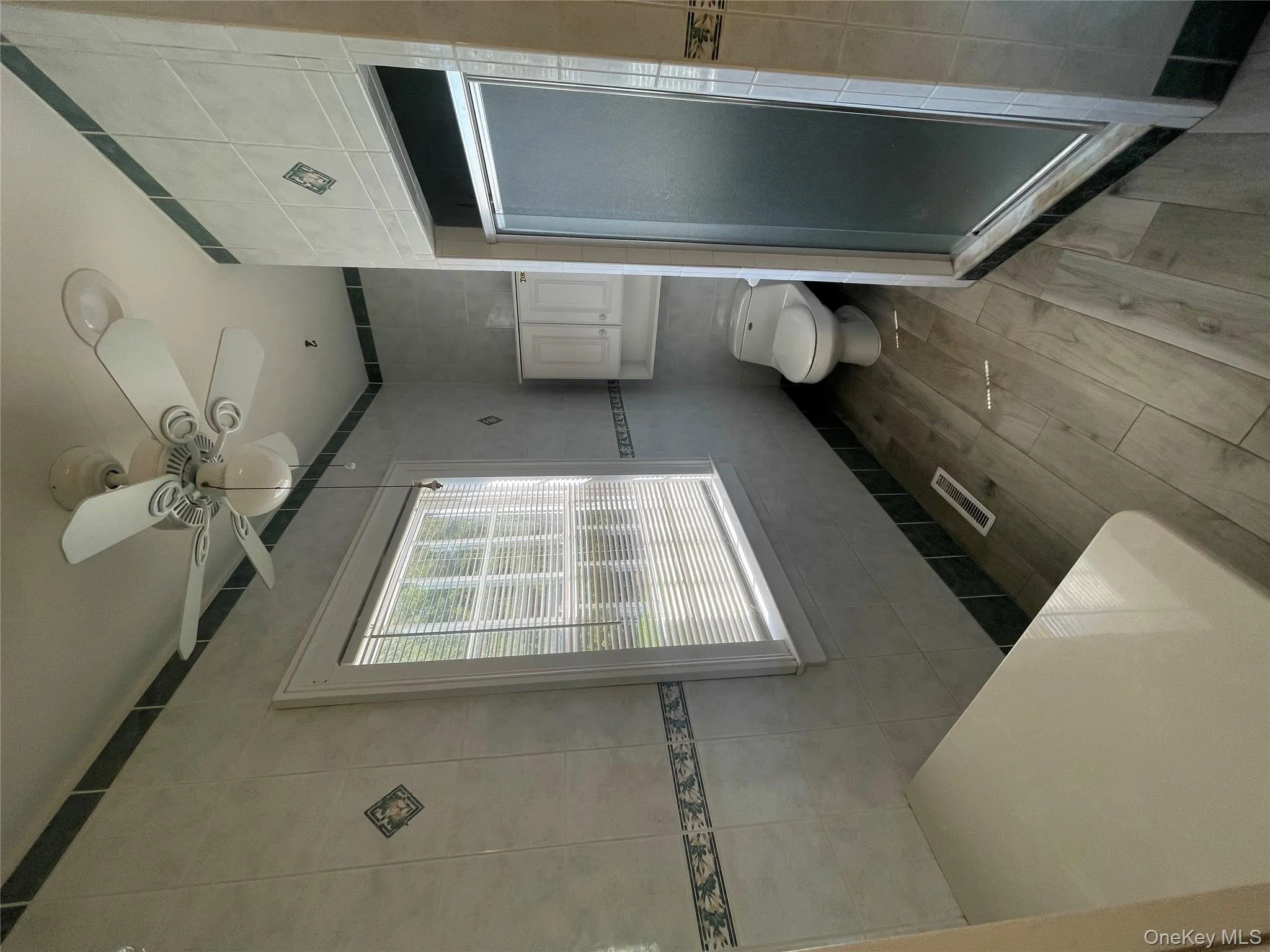 Full bathroom with tile walls, a shower stall, a ceiling fan, and wood finished floors Full bathroom with tile walls, a shower stall, a ceiling fan, and wood finished floors