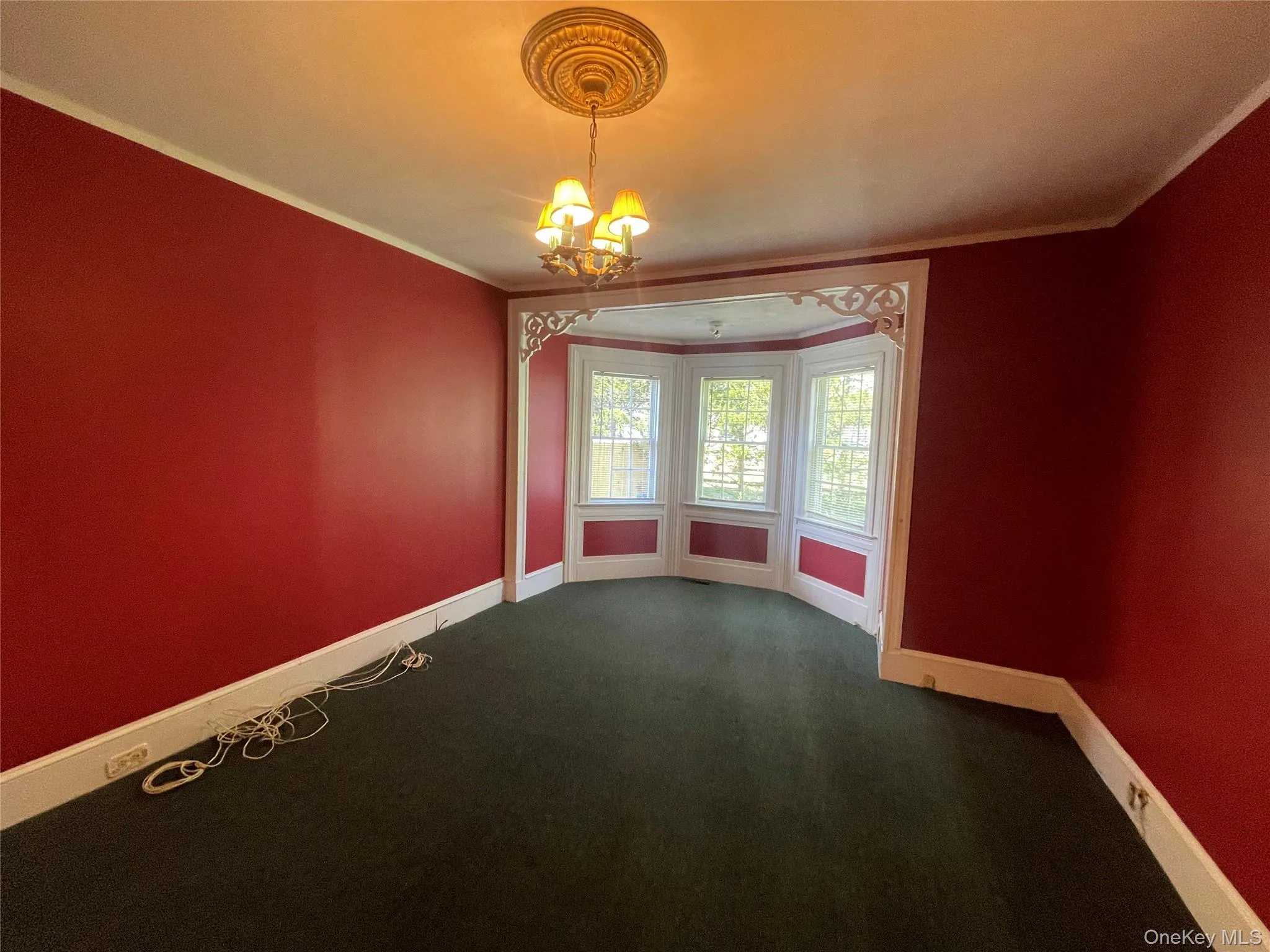 Empty room with a chandelier, dark colored carpet, and crown molding Empty room with a chandelier, dark colored carpet, and crown molding