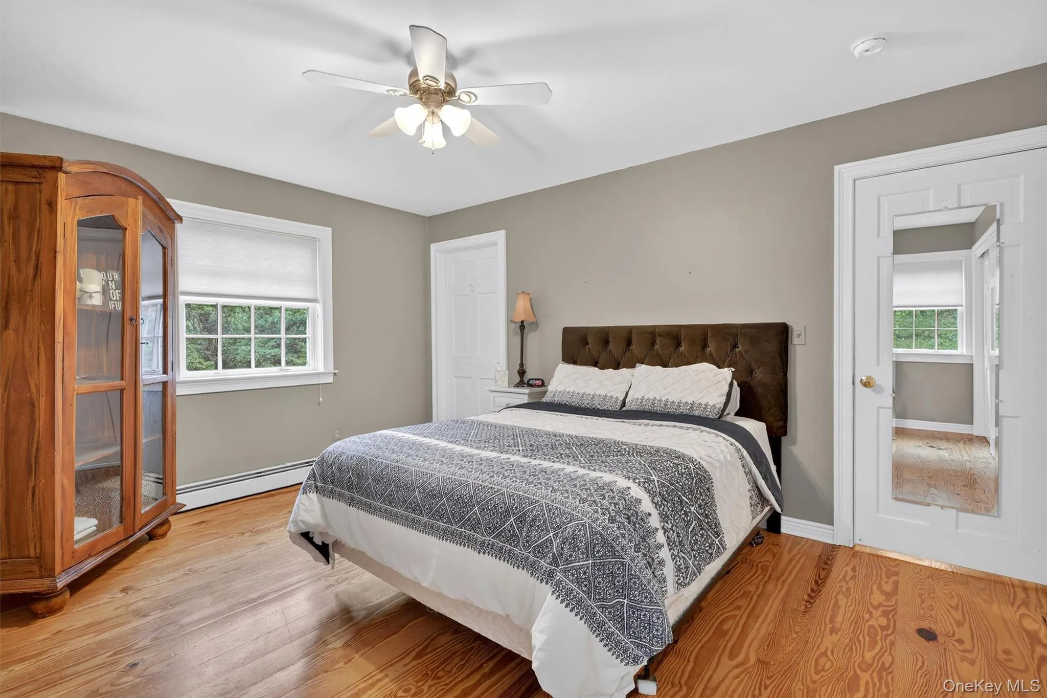 Bedroom featuring baseboard heating, multiple windows, wood finished floors, and ceiling fan Bedroom featuring baseboard heating, multiple windows, wood finished floors, and ceiling fan