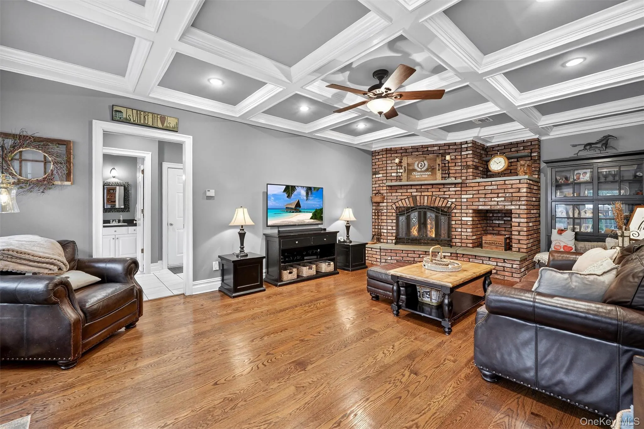 Living room featuring ceiling fan, a fireplace, beamed ceiling, wood finished floors, and coffered ceiling Living room featuring ceiling fan, a fireplace, beamed ceiling, wood finished floors, and coffered ceiling