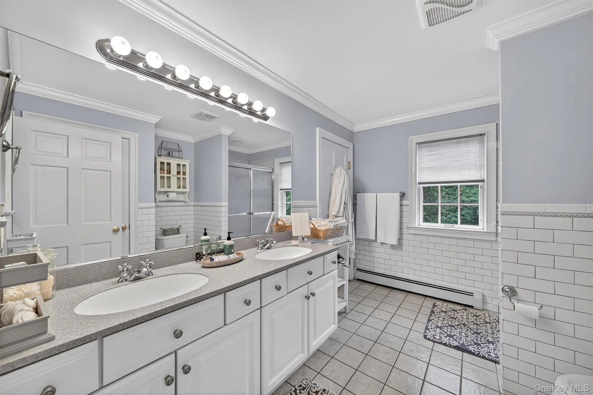 Full bath with a baseboard radiator, tile walls, a wainscoted wall, tile patterned flooring, and double vanity Full bath with a baseboard radiator, tile walls, a wainscoted wall, tile patterned flooring, and double vanity