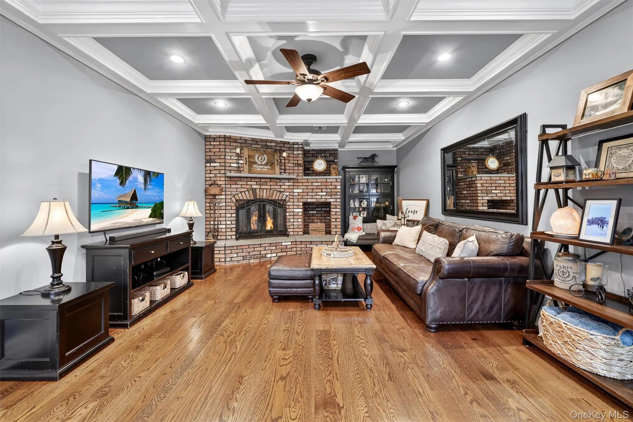 Living area with a ceiling fan, light wood finished floors, a fireplace, coffered ceiling, and beamed ceiling Living area with a ceiling fan, light wood finished floors, a fireplace, coffered ceiling, and beamed ceiling