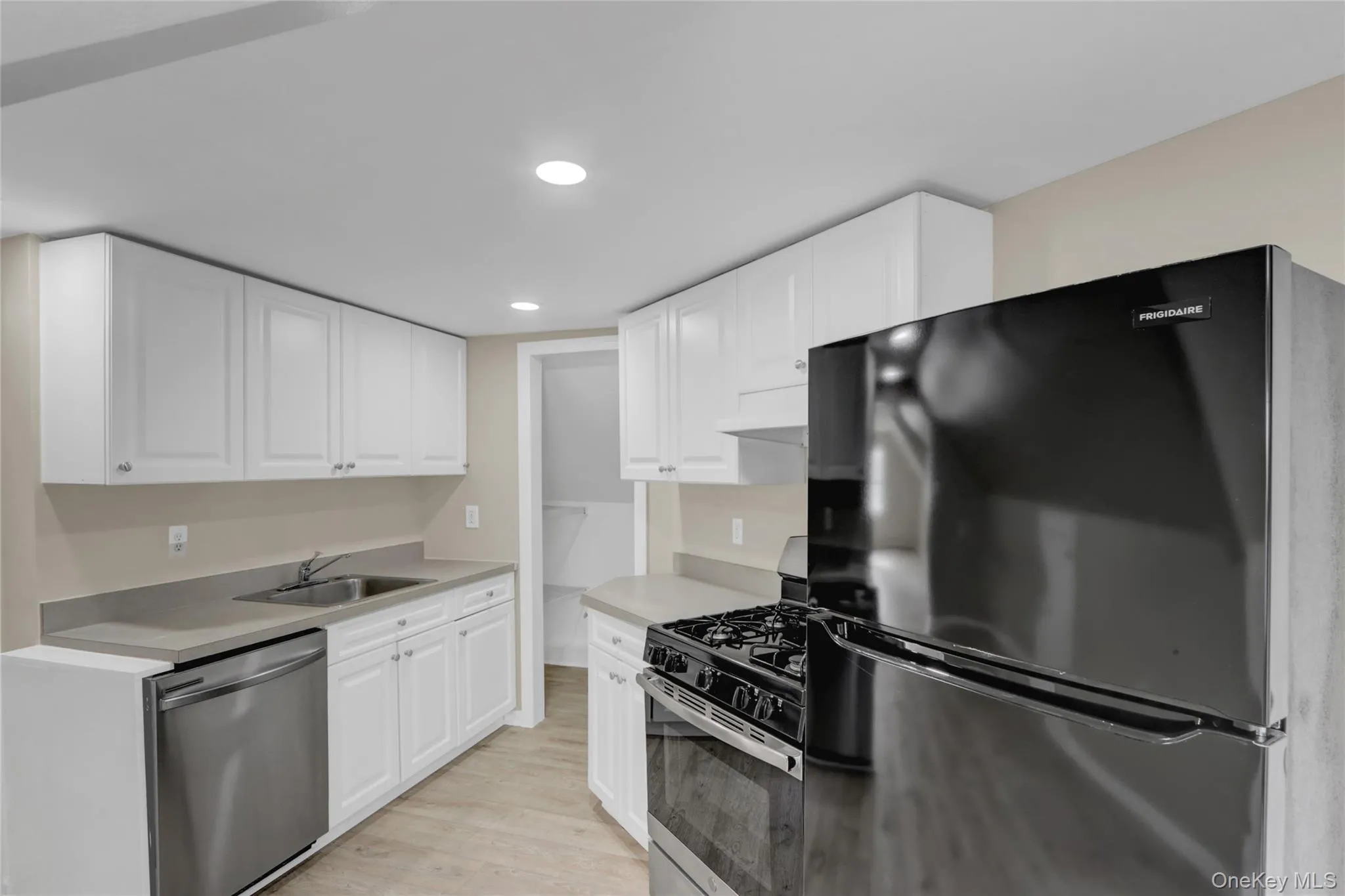 Kitchen with a sink, stainless steel appliances, white cabinets, light wood-style floors, and under cabinet range hood Kitchen with a sink, stainless steel appliances, white cabinets, light wood-style floors, and under cabinet range hood