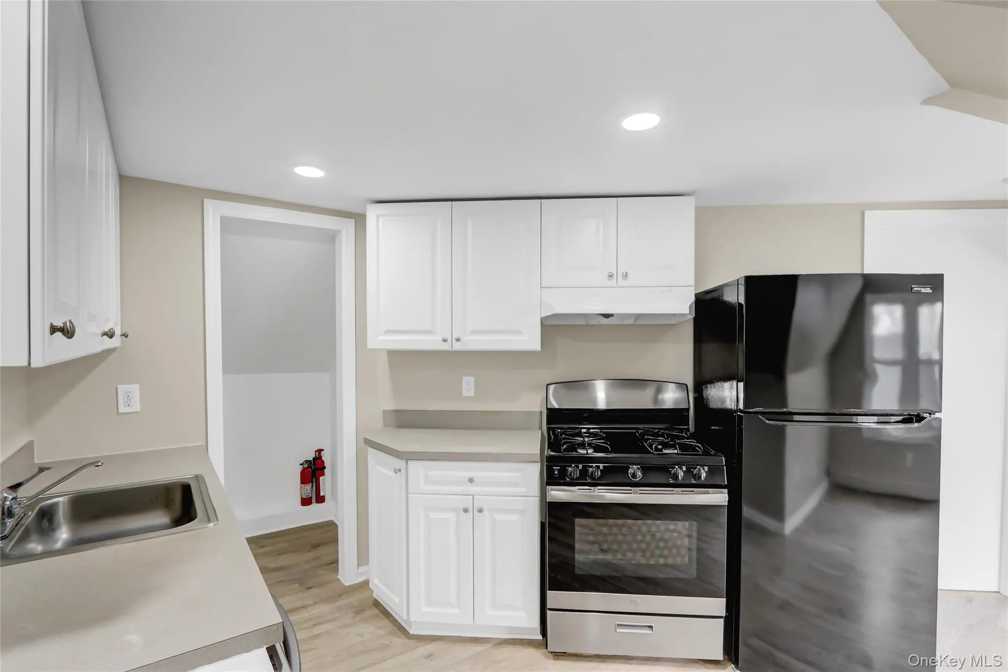 Kitchen featuring under cabinet range hood, gas range, light countertops, freestanding refrigerator, and a sink Kitchen featuring under cabinet range hood, gas range, light countertops, freestanding refrigerator, and a sink