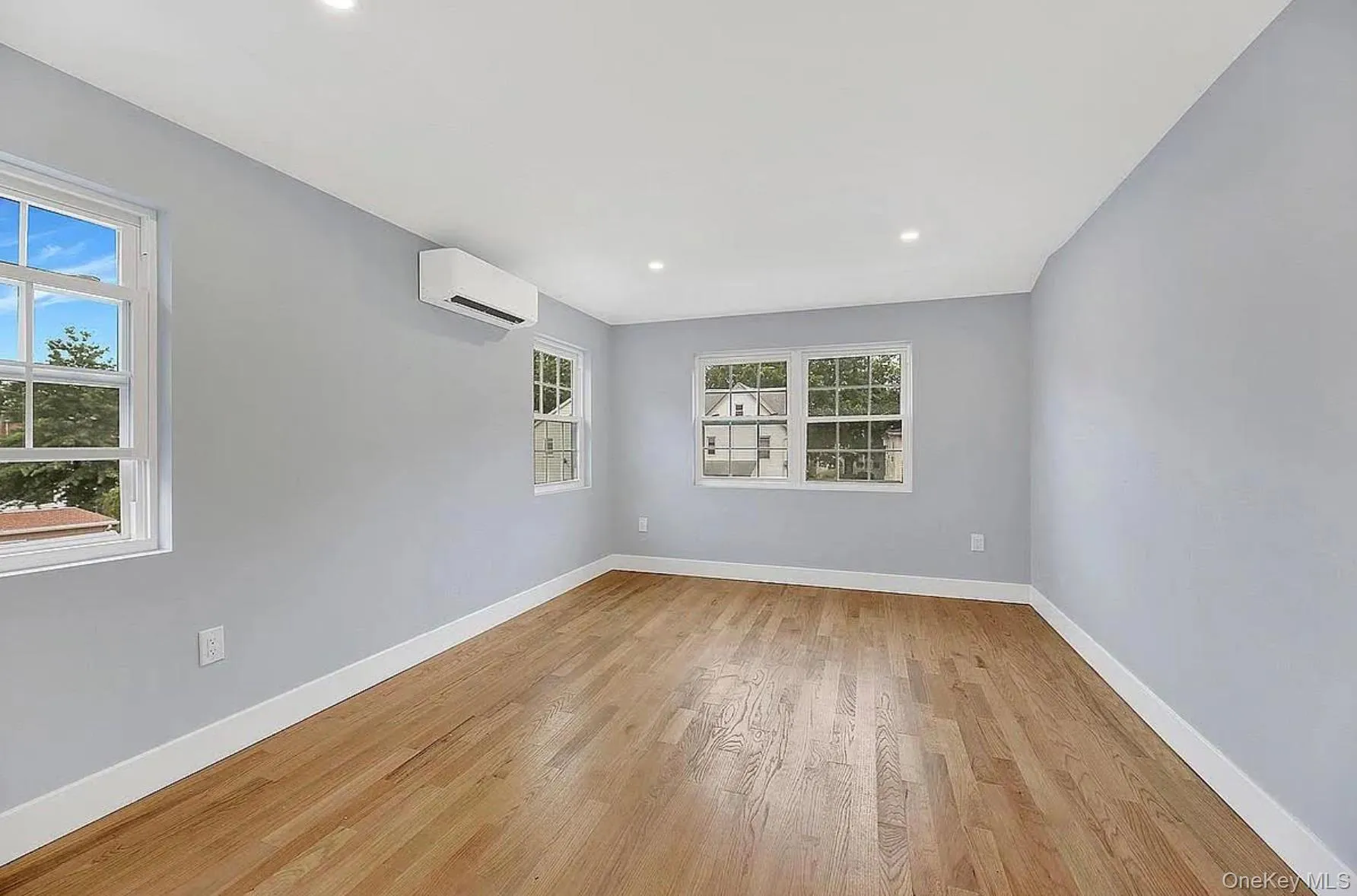 Empty room with a wall mounted air conditioner, light wood-type flooring, baseboards, and recessed lighting Empty room with a wall mounted air conditioner, light wood-type flooring, baseboards, and recessed lighting