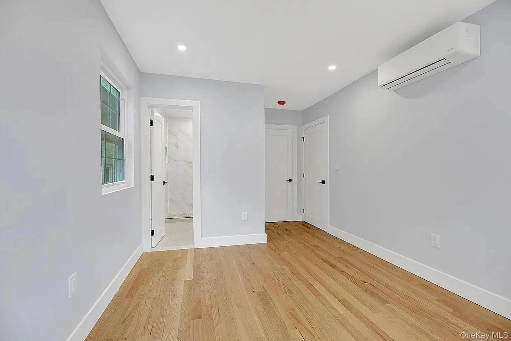 Unfurnished bedroom with a wall unit AC, light wood-style floors, baseboards, ensuite bathroom, and recessed lighting Unfurnished bedroom with a wall unit AC, light wood-style floors, baseboards, ensuite bathroom, and recessed lighting