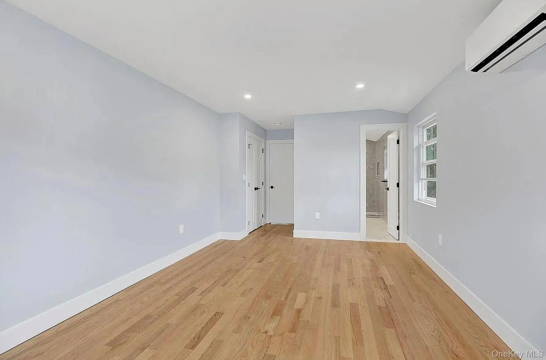 Empty room with a wall mounted air conditioner, light wood-style flooring, baseboards, and recessed lighting Empty room with a wall mounted air conditioner, light wood-style flooring, baseboards, and recessed lighting