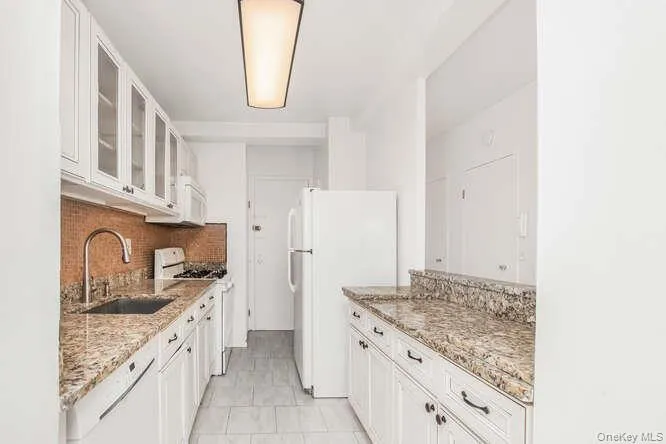 Kitchen with glass insert cabinets, white cabinetry, white appliances, and light stone counters Kitchen with glass insert cabinets, white cabinetry, white appliances, and light stone counters
