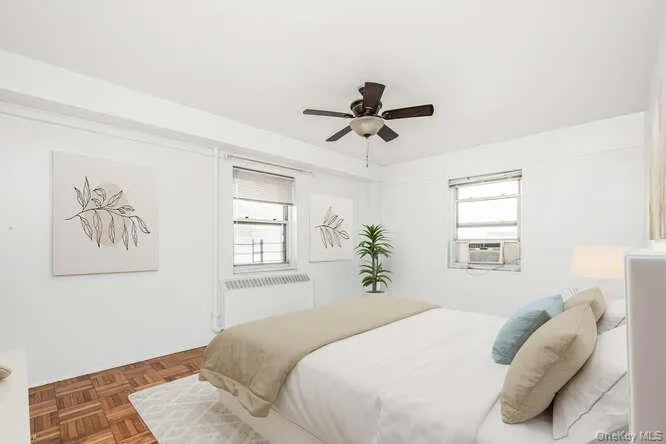 Virtually staged Primary Bedroom featuring multiple windows, a ceiling fan, and radiator heating unit Virtually staged Primary Bedroom featuring multiple windows, a ceiling fan, and radiator heating unit
