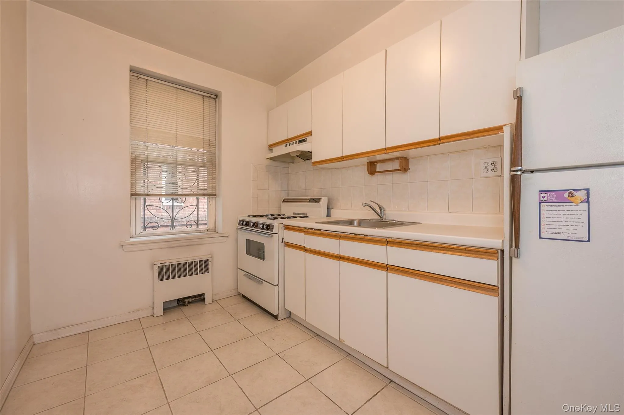 Kitchen featuring white appliances, light countertops, decorative backsplash, radiator, and dual tone cabinetry Kitchen featuring white appliances, light countertops, decorative backsplash, radiator, and dual tone cabinetry