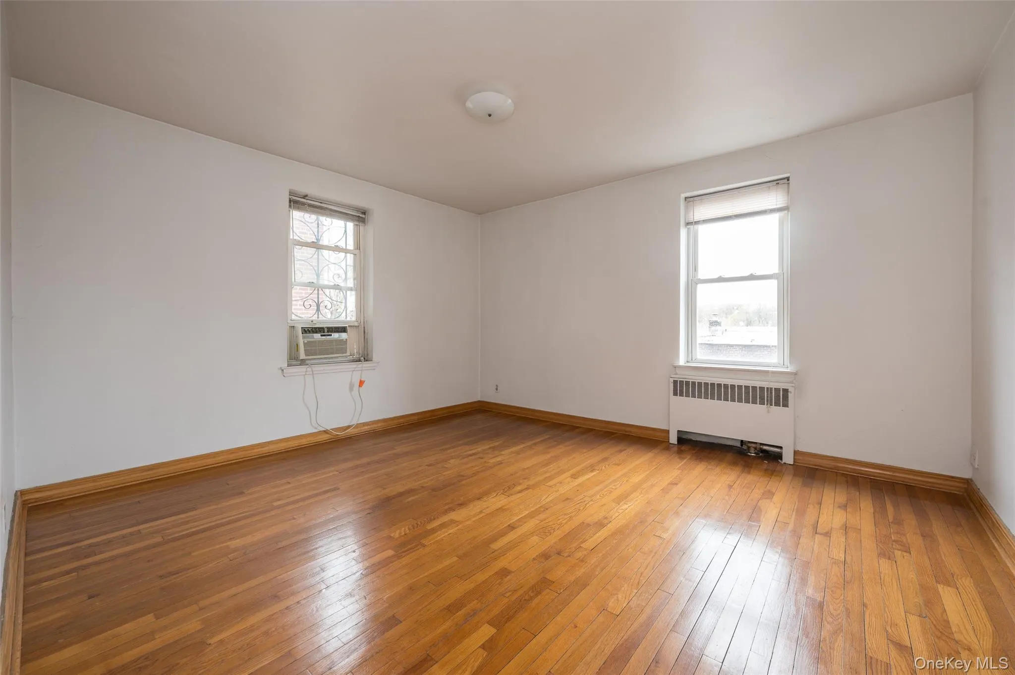 Unfurnished room with radiator, light wood-style flooring, healthy amount of natural light, and cooling unit Unfurnished room with radiator, light wood-style flooring, healthy amount of natural light, and cooling unit