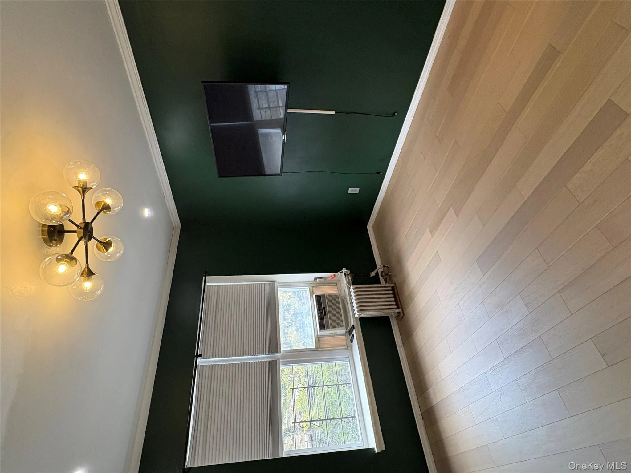 Unfurnished room featuring radiator, ornamental molding, light wood-type flooring, cooling unit, and hanging lights Unfurnished room featuring radiator, ornamental molding, light wood-type flooring, cooling unit, and hanging lights