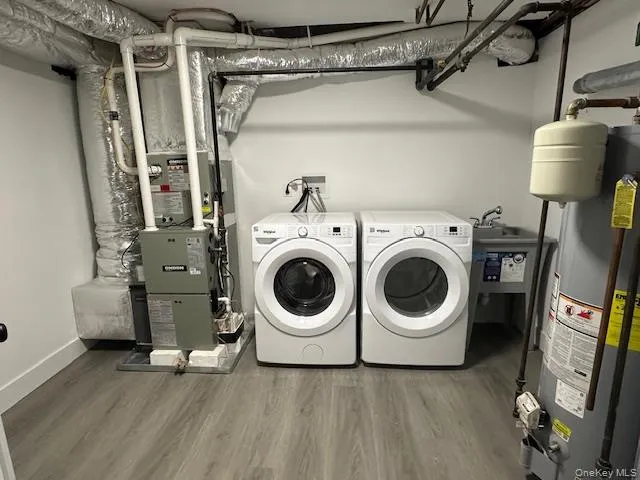 Laundry area with water heater, light wood-style flooring, and separate washer and dryer Laundry area with water heater, light wood-style flooring, and separate washer and dryer
