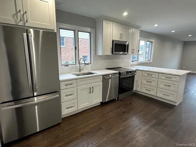 Kitchen featuring stainless steel appliances, a peninsula, dark wood finished floors, white cabinetry, and decorative backsplash Kitchen featuring stainless steel appliances, a peninsula, dark wood finished floors, white cabinetry, and decorative backsplash