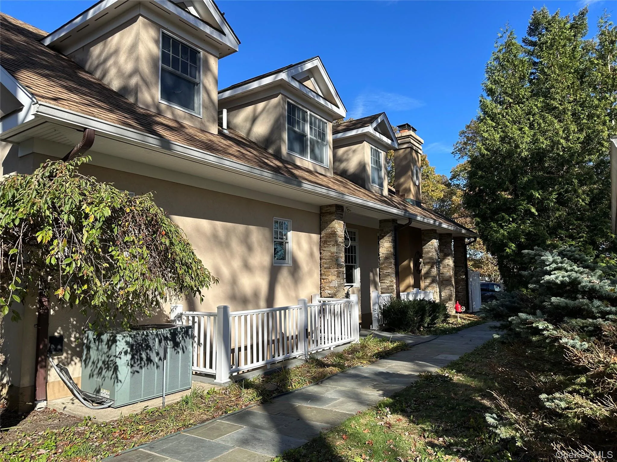 View of side of home featuring stucco facade, covered outside entrance stairs, a chimney, and stone accents View of side of home featuring stucco facade, covered outside entrance stairs, a chimney, and stone accents