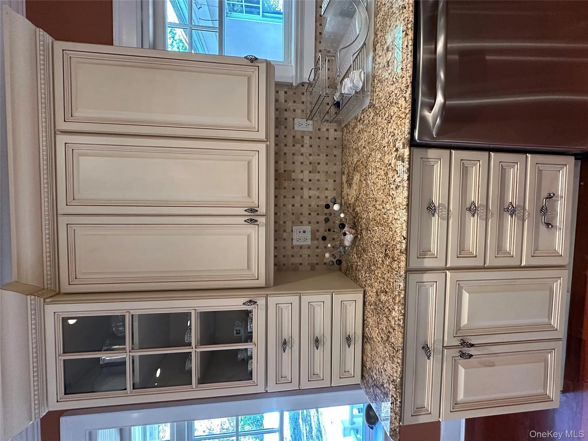 Kitchen with dishwashing machine, light stone countertops, decorative backsplash, cream cabinets, and glass insert cabinets Kitchen with dishwashing machine, light stone countertops, decorative backsplash, cream cabinets, and glass insert cabinets