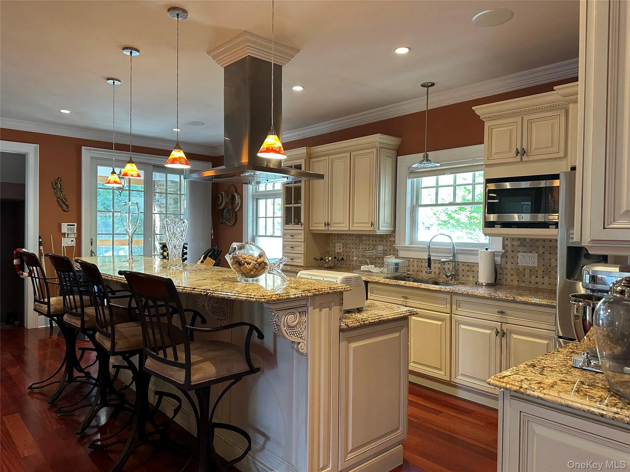 Kitchen with custom cabinetry, light granite countertops, Turkish marble mosaic backsplash, crown molding, and island range hood Kitchen with custom cabinetry, light granite countertops, Turkish marble mosaic backsplash, crown molding, and island range hood