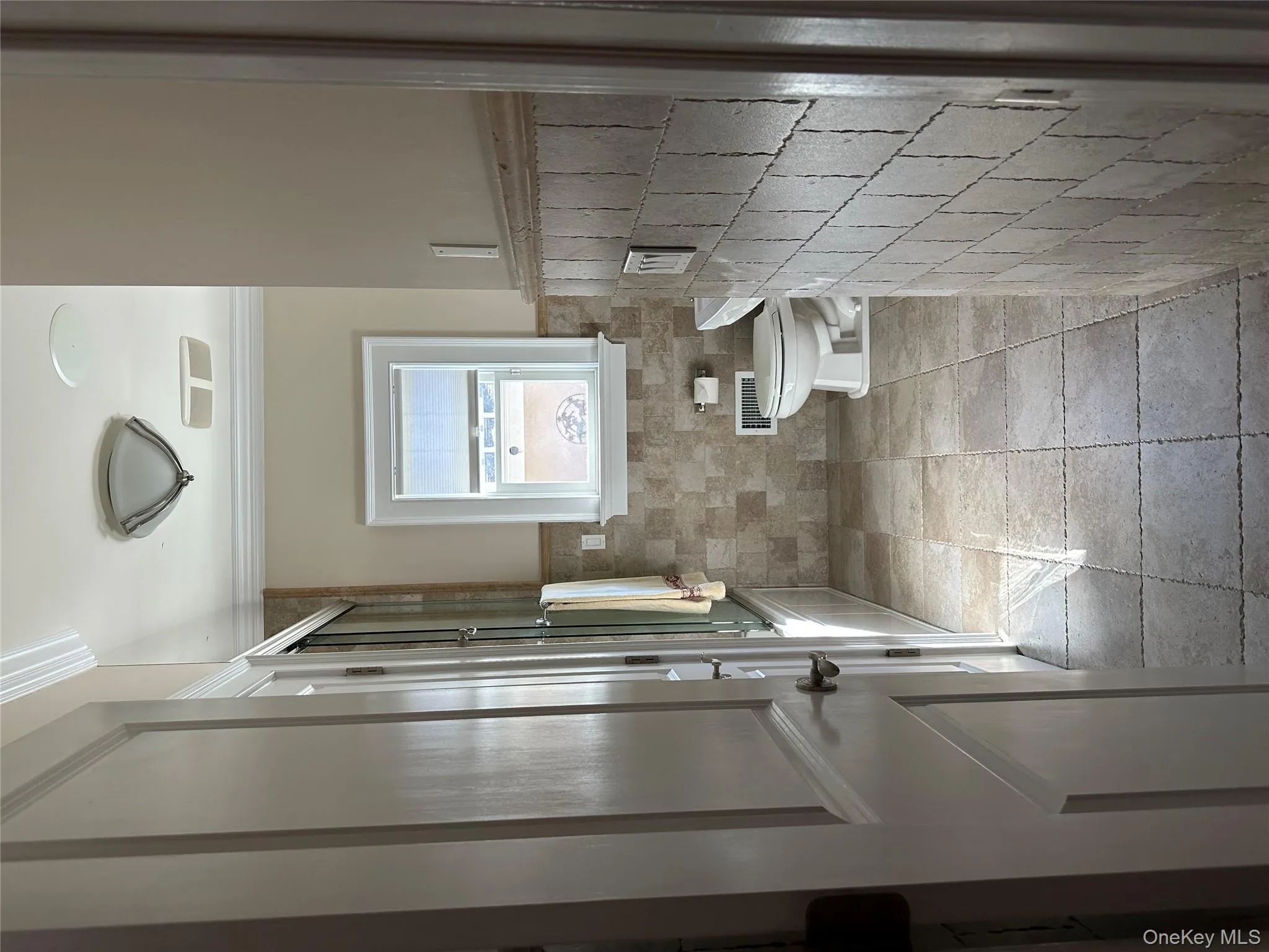 Bathroom with bath / shower combo with glass door, ornamental molding, tile walls, wainscoting, and light tile patterned floors Bathroom with bath / shower combo with glass door, ornamental molding, tile walls, wainscoting, and light tile patterned floors