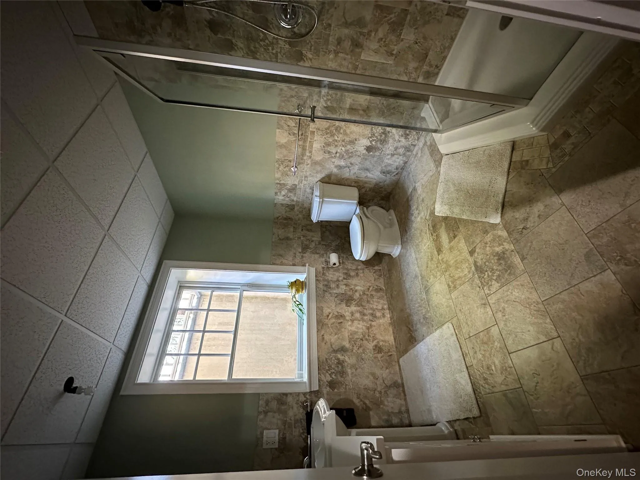 Full bathroom with a wainscoted wall, tile walls, a stall shower, a paneled ceiling, and stone tile floors Full bathroom with a wainscoted wall, tile walls, a stall shower, a paneled ceiling, and stone tile floors