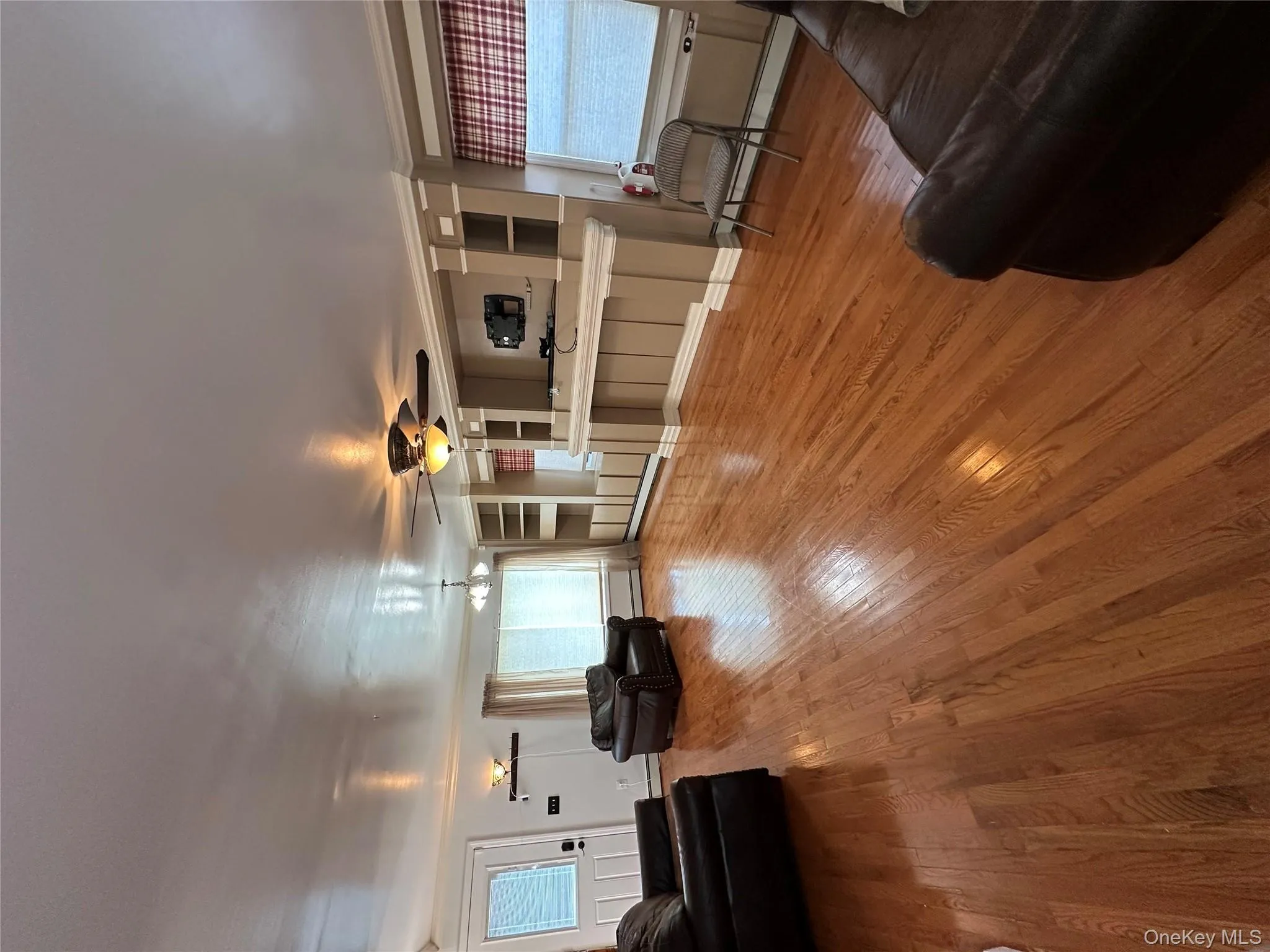 Living room with baseboard heating, wood finished floors, a ceiling fan, and built in shelves Living room with baseboard heating, wood finished floors, a ceiling fan, and built in shelves