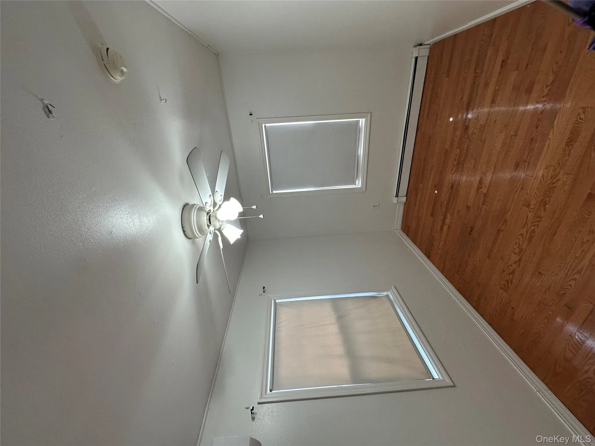 Unfurnished room featuring a baseboard heating unit, a ceiling fan, a smoke detector, and wood finished floors Unfurnished room featuring a baseboard heating unit, a ceiling fan, a smoke detector, and wood finished floors