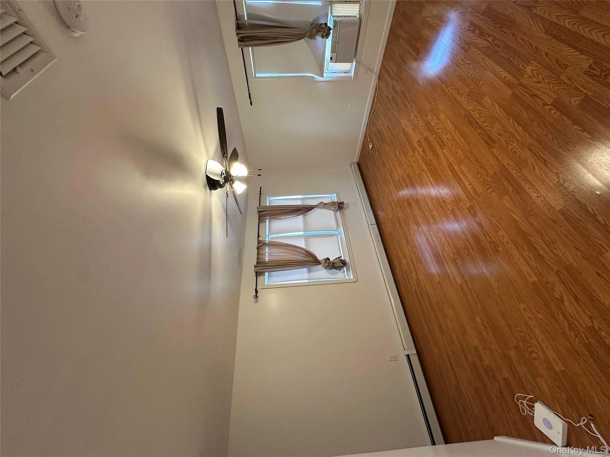 Empty room featuring a baseboard heating unit, ceiling fan, wood finished floors, and a smoke detector Empty room featuring a baseboard heating unit, ceiling fan, wood finished floors, and a smoke detector