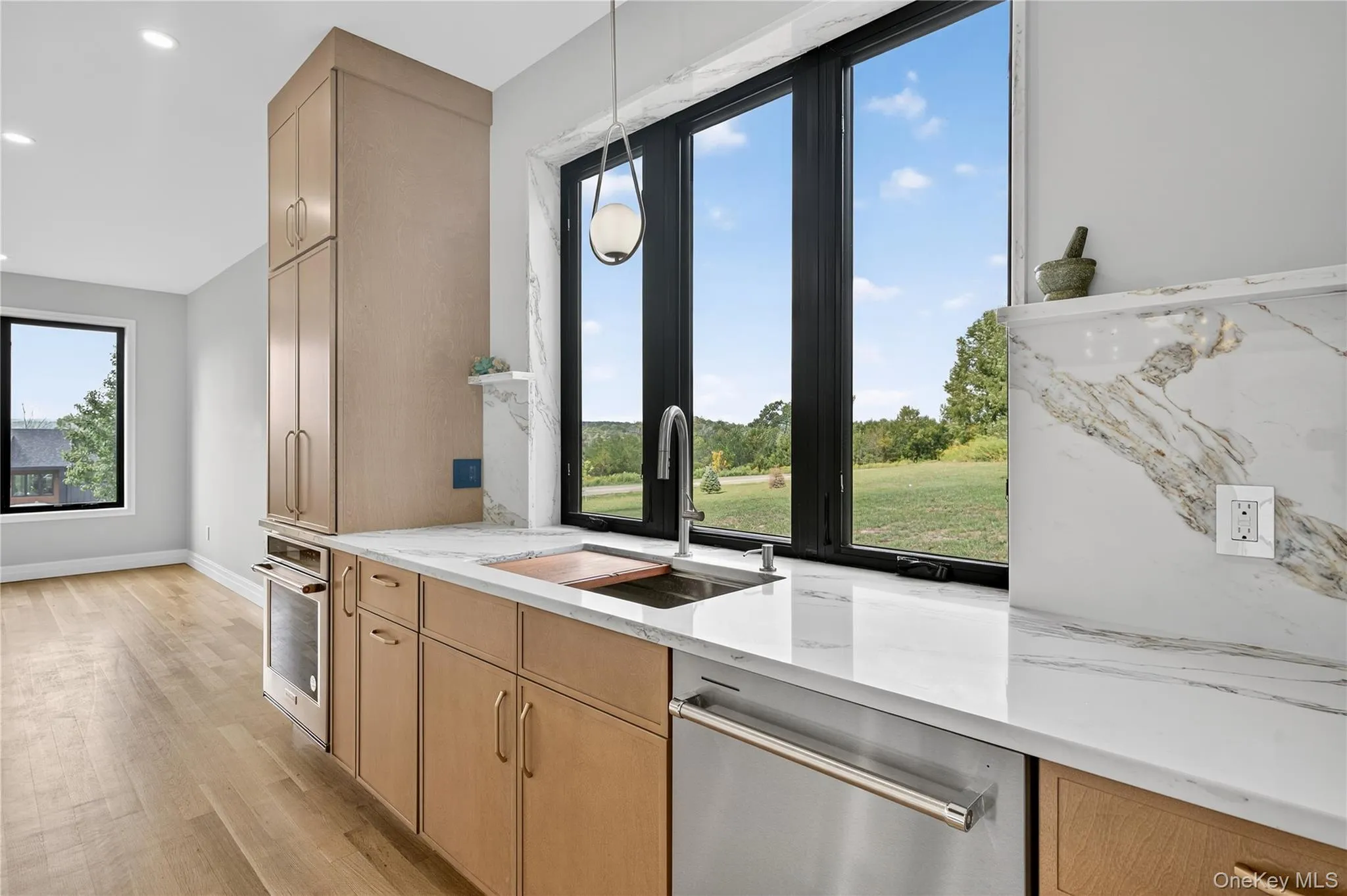 Kitchen with light stone counters, appliances with stainless steel finishes, light wood-style floors, pendant lighting, and light brown cabinetry Kitchen with light stone counters, appliances with stainless steel finishes, light wood-style floors, pendant lighting, and light brown cabinetry