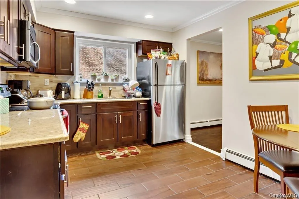 Kitchen featuring stainless steel appliances, wood finish floors, ornamental molding, a baseboard radiator, and light stone counters Kitchen featuring stainless steel appliances, wood finish floors, ornamental molding, a baseboard radiator, and light stone counters