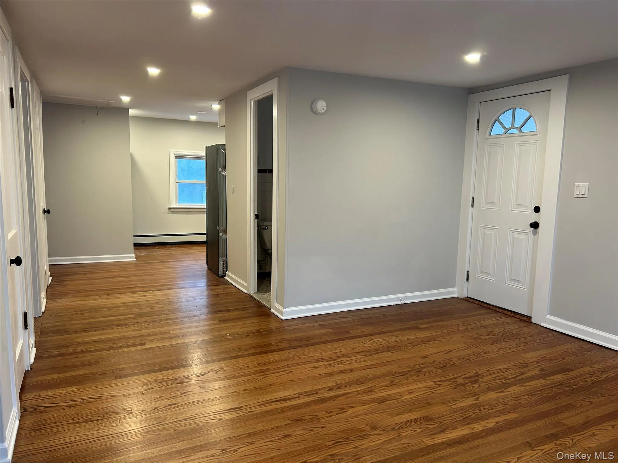 Living room featuring dark wood-style floors, plenty of natural light, recessed lighting, and baseboard heating Living room featuring dark wood-style floors, plenty of natural light, recessed lighting, and baseboard heating