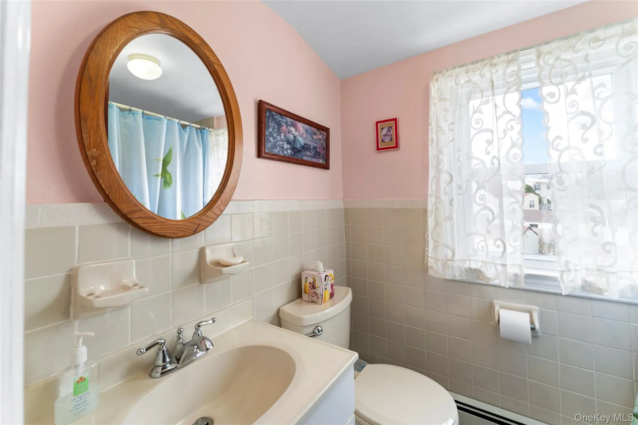 Bathroom with vanity, a baseboard heating unit, curtained shower, tile walls, and wainscoting Bathroom with vanity, a baseboard heating unit, curtained shower, tile walls, and wainscoting