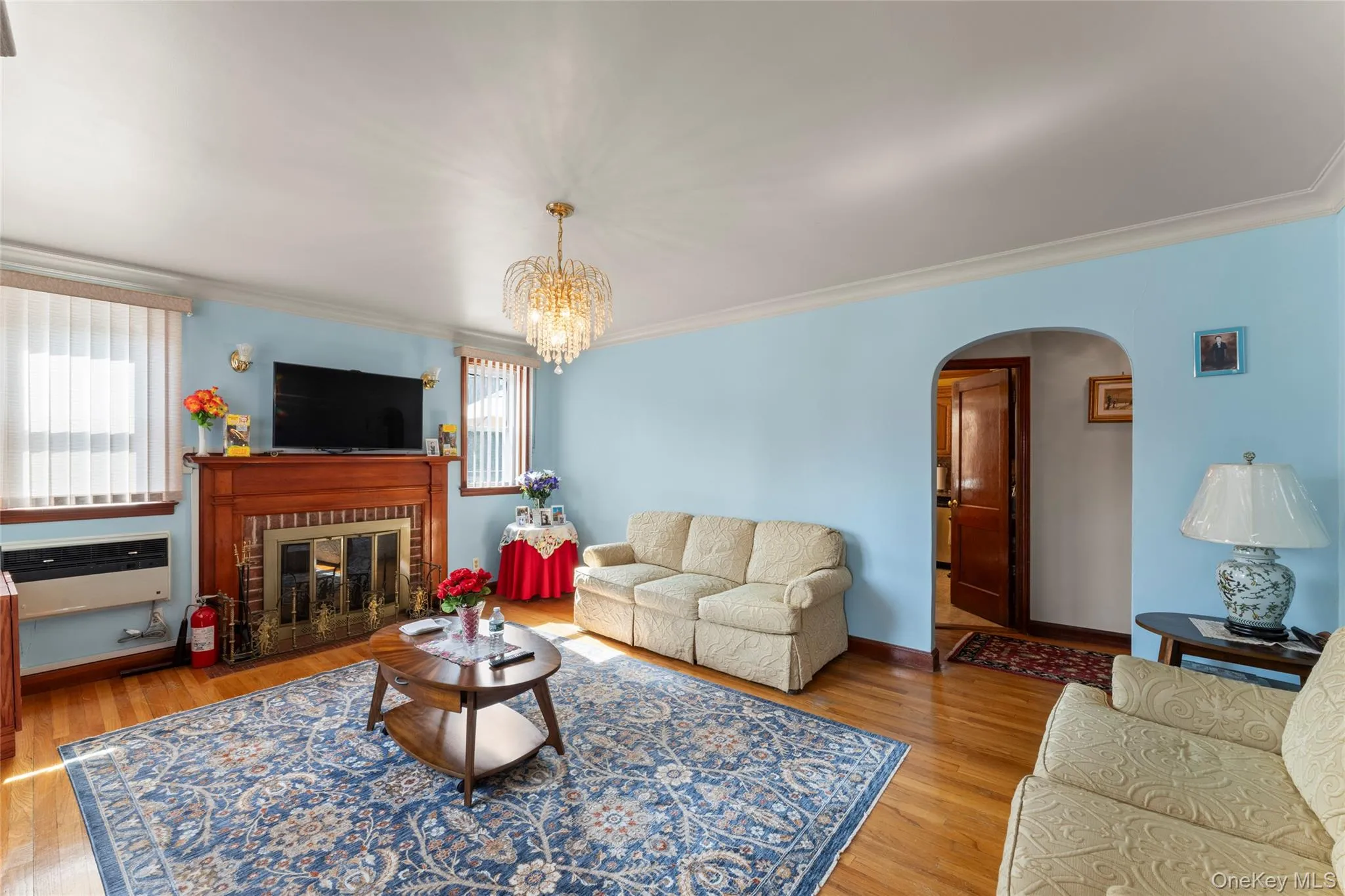 Living room with wood finished floors, arched walkways, a chandelier, ornamental molding, and a fireplace Living room with wood finished floors, arched walkways, a chandelier, ornamental molding, and a fireplace