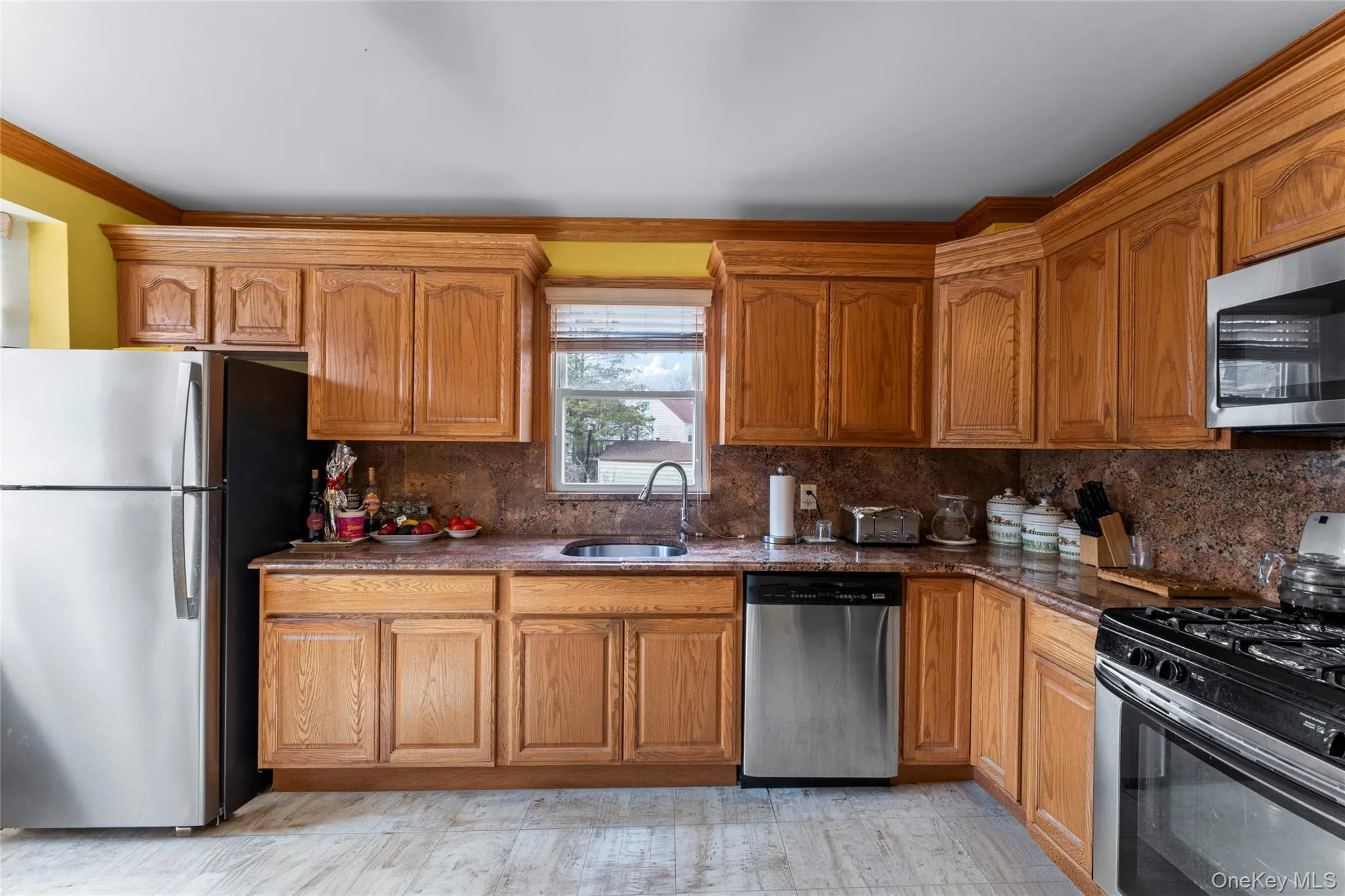 Kitchen featuring stainless steel appliances, wood finish cabinets, backsplash, dark stone counters, and crown molding Kitchen featuring stainless steel appliances, wood finish cabinets, backsplash, dark stone counters, and crown molding