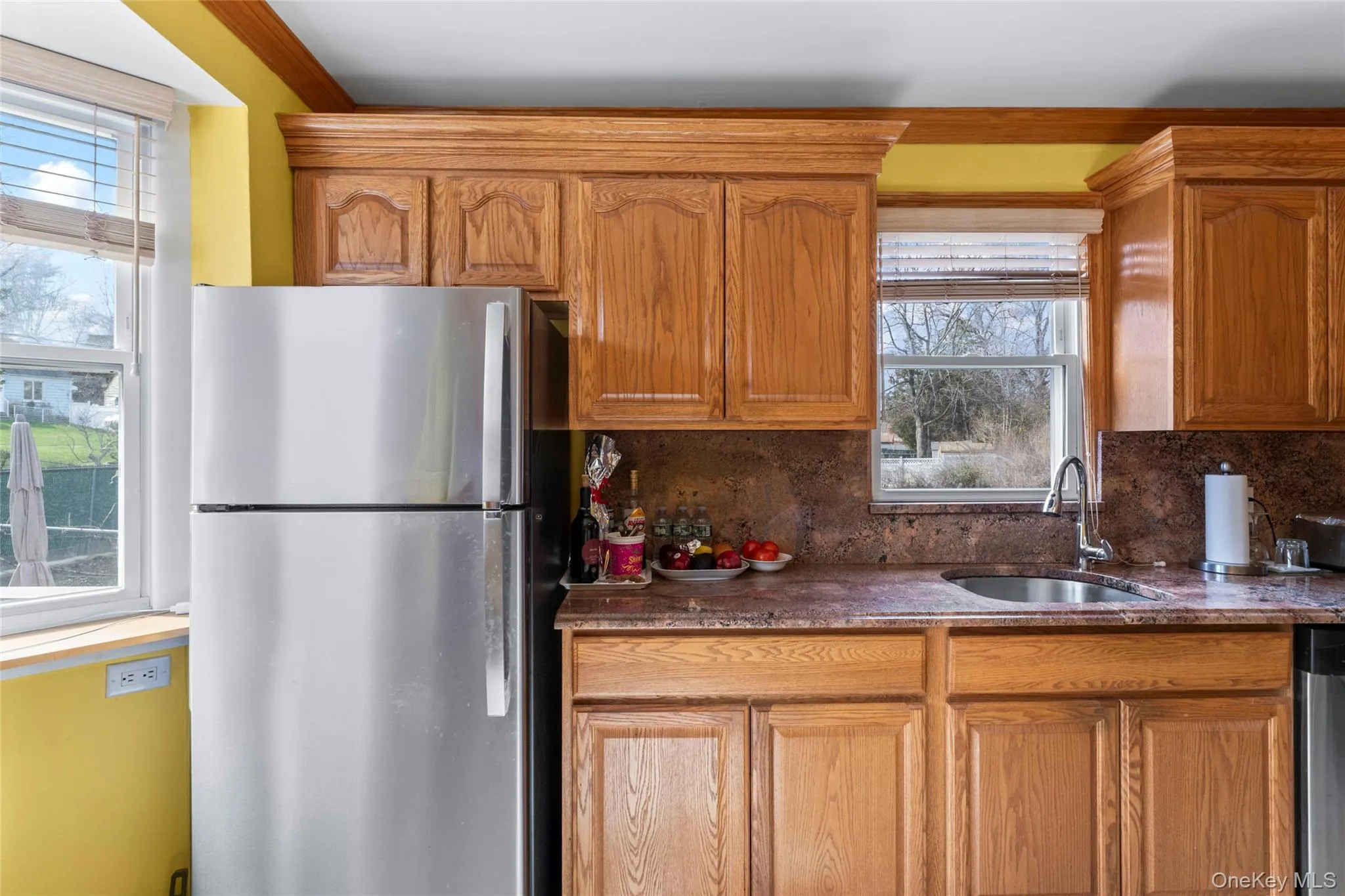 Kitchen with stainless steel appliances, tasteful backsplash, wood finish cabinetry, and dark stone countertops Kitchen with stainless steel appliances, tasteful backsplash, wood finish cabinetry, and dark stone countertops