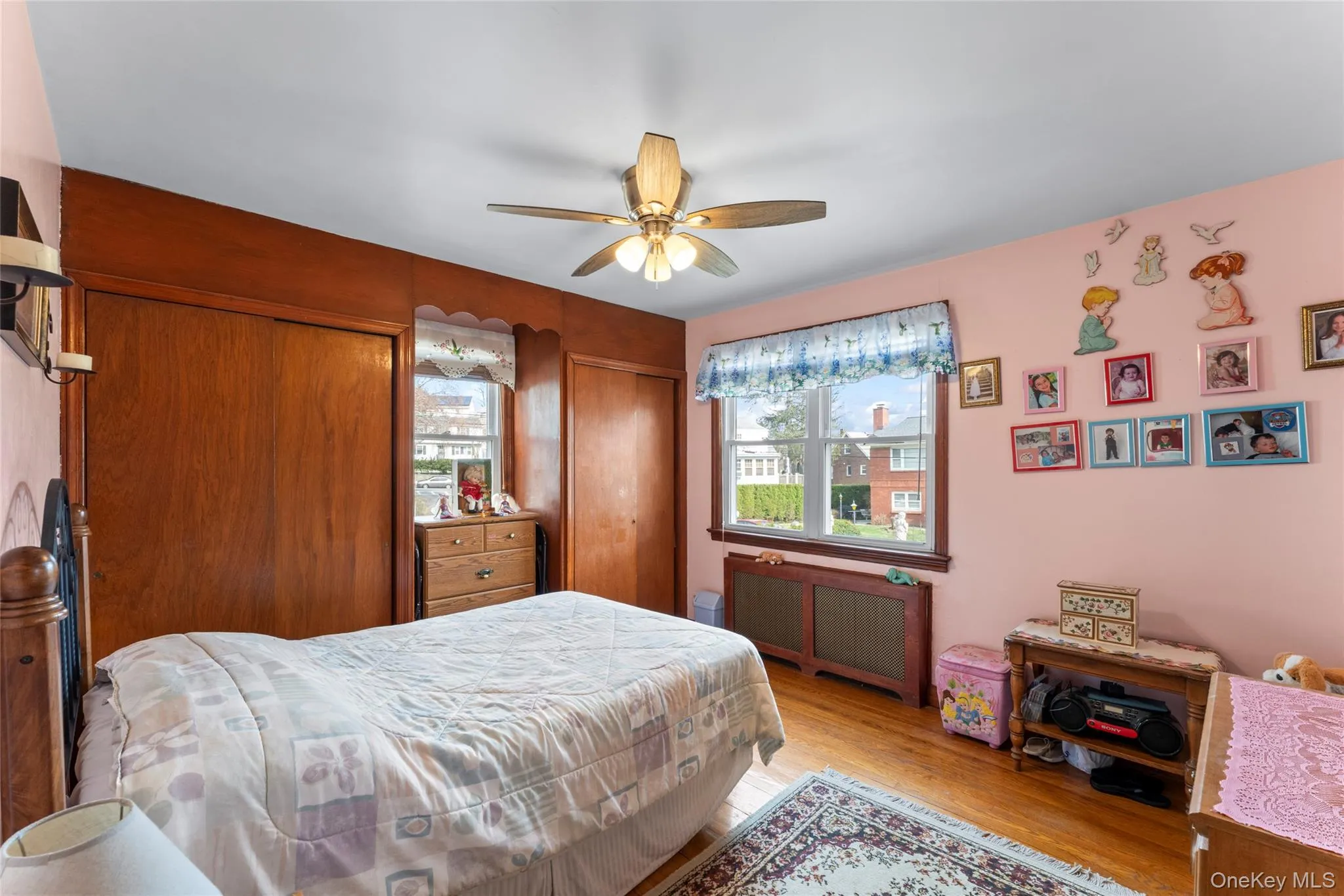 Bedroom with multiple closets, radiator heating unit, light wood-type flooring, and ceiling fan Bedroom with multiple closets, radiator heating unit, light wood-type flooring, and ceiling fan