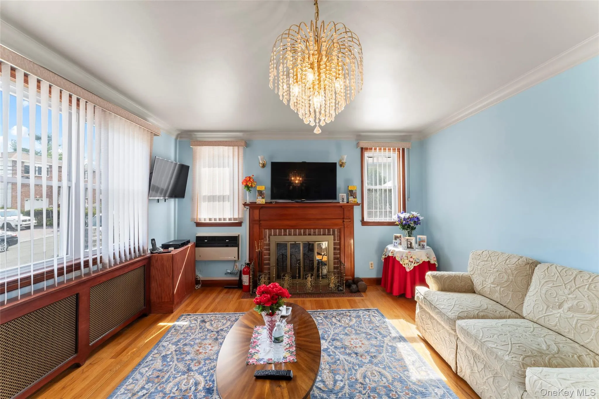 Living room with ornamental molding, light wood-style floors, a brick fireplace, hanging lights, and radiator Living room with ornamental molding, light wood-style floors, a brick fireplace, hanging lights, and radiator