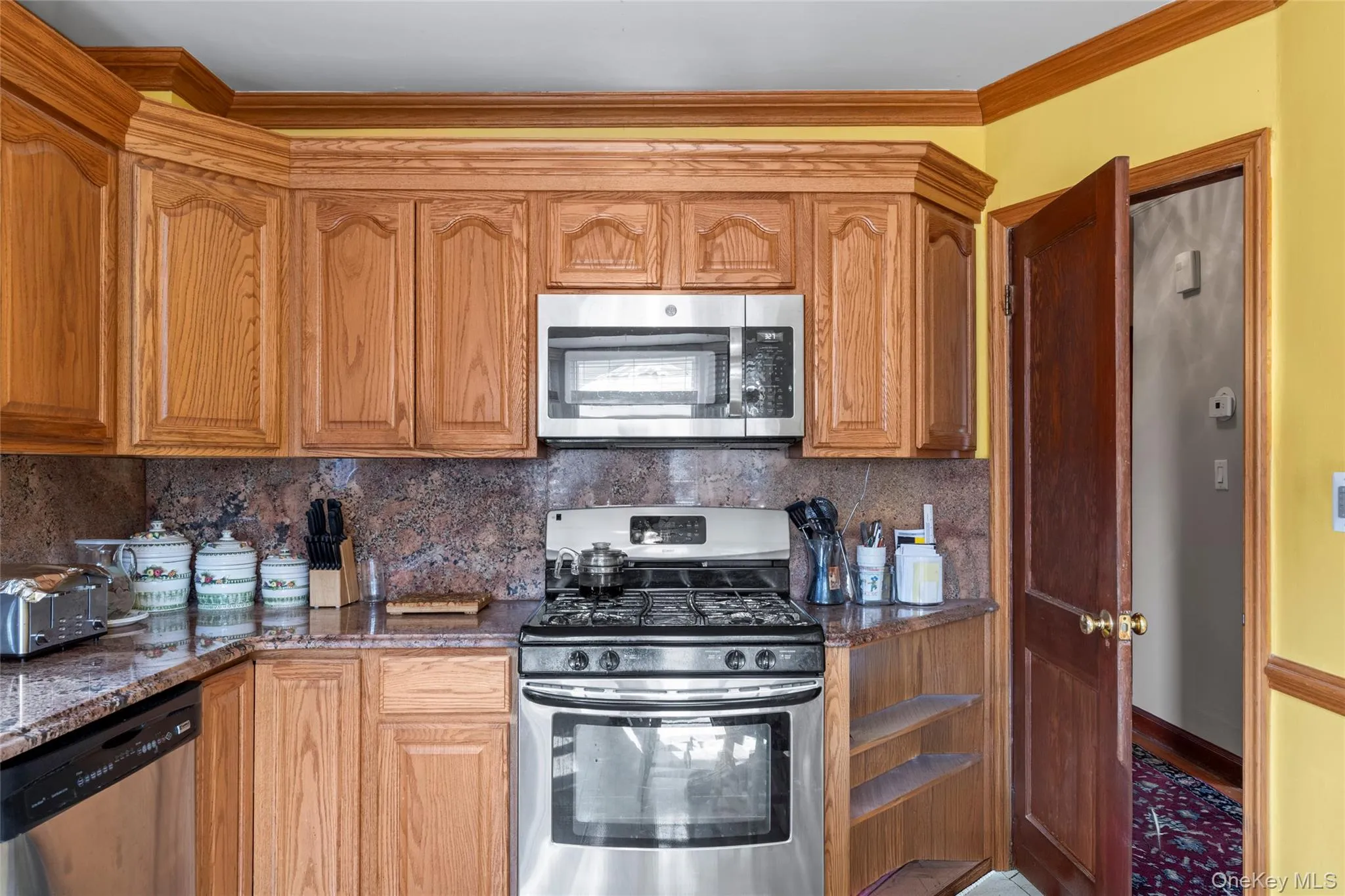 Kitchen featuring stainless steel appliances, crown molding, backsplash, and wood finish cabinets Kitchen featuring stainless steel appliances, crown molding, backsplash, and wood finish cabinets