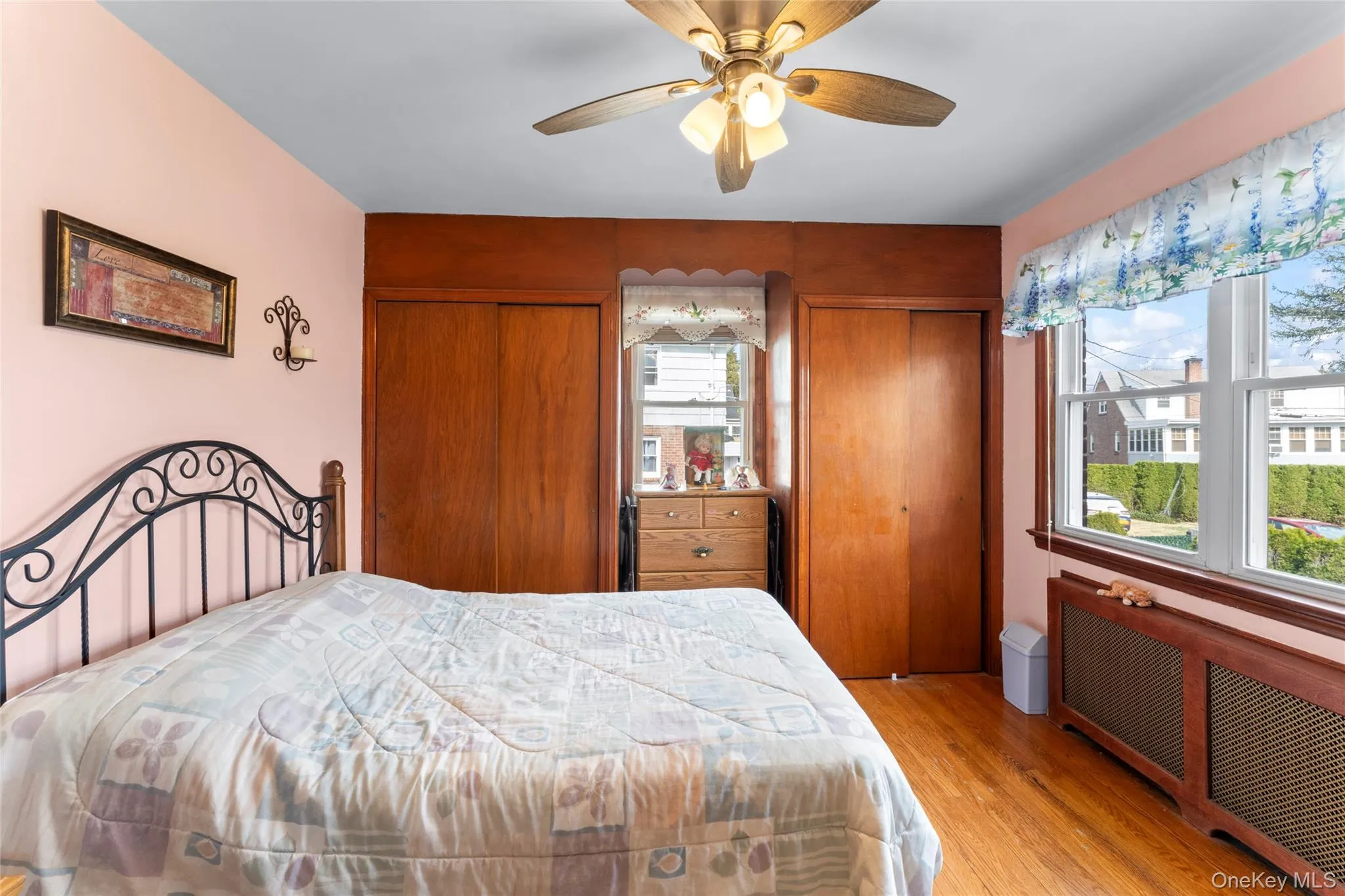 Bedroom with two closets, radiator, light wood finished floors, and a ceiling fan Bedroom with two closets, radiator, light wood finished floors, and a ceiling fan
