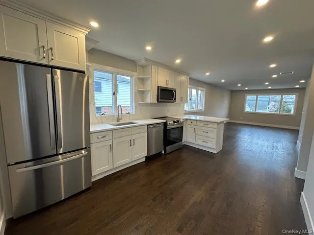 Kitchen featuring stainless steel appliances, white cabinets, light countertops, a peninsula, and dark wood-style flooring Kitchen featuring stainless steel appliances, white cabinets, light countertops, a peninsula, and dark wood-style flooring