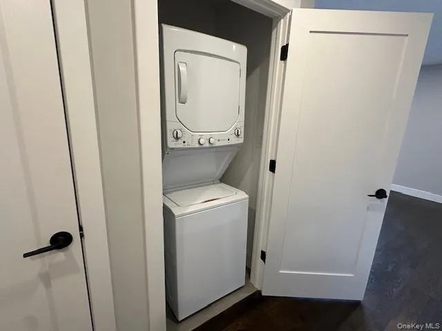 Laundry area with dark wood finished floors and stacked washing machine and dryer Laundry area with dark wood finished floors and stacked washing machine and dryer