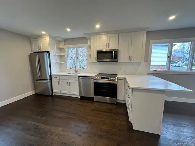 Kitchen featuring a peninsula, stainless steel appliances, open shelves, white cabinetry, and dark wood-style floors Kitchen featuring a peninsula, stainless steel appliances, open shelves, white cabinetry, and dark wood-style floors