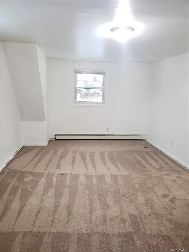 Additional living space featuring light colored carpet and a baseboard heating unit Additional living space featuring light colored carpet and a baseboard heating unit
