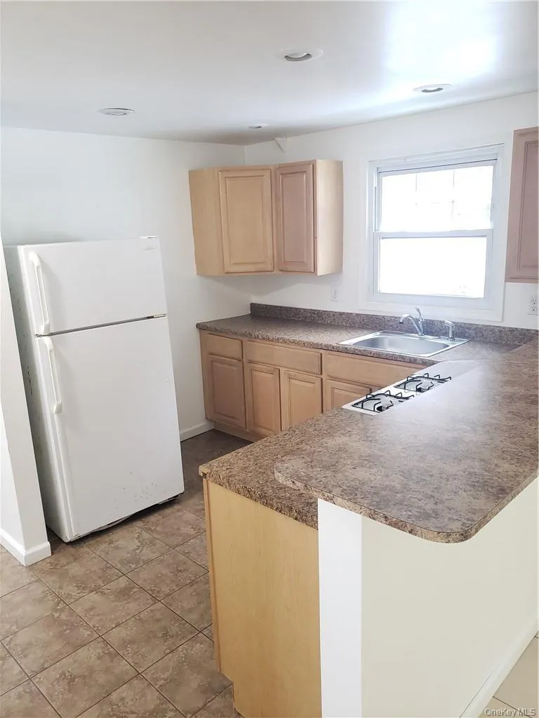 Kitchen featuring dark countertops, freestanding refrigerator, a peninsula, and light wood finish cabinets Kitchen featuring dark countertops, freestanding refrigerator, a peninsula, and light wood finish cabinets