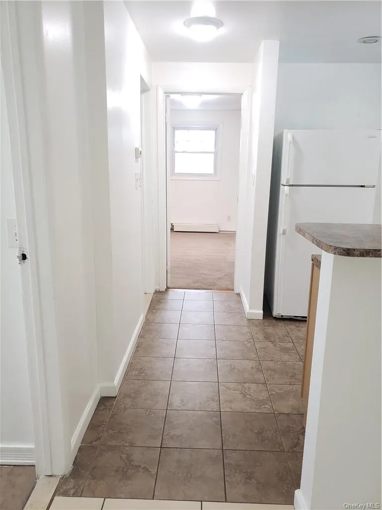 Hallway featuring light tile patterned flooring and a baseboard radiator Hallway featuring light tile patterned flooring and a baseboard radiator