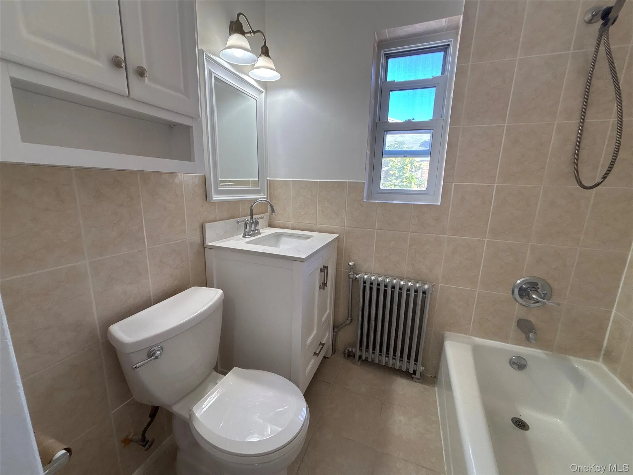 Full bath with shower / washtub combination, vanity, radiator, tile walls, and light tile patterned floors Full bath with shower / washtub combination, vanity, radiator, tile walls, and light tile patterned floors