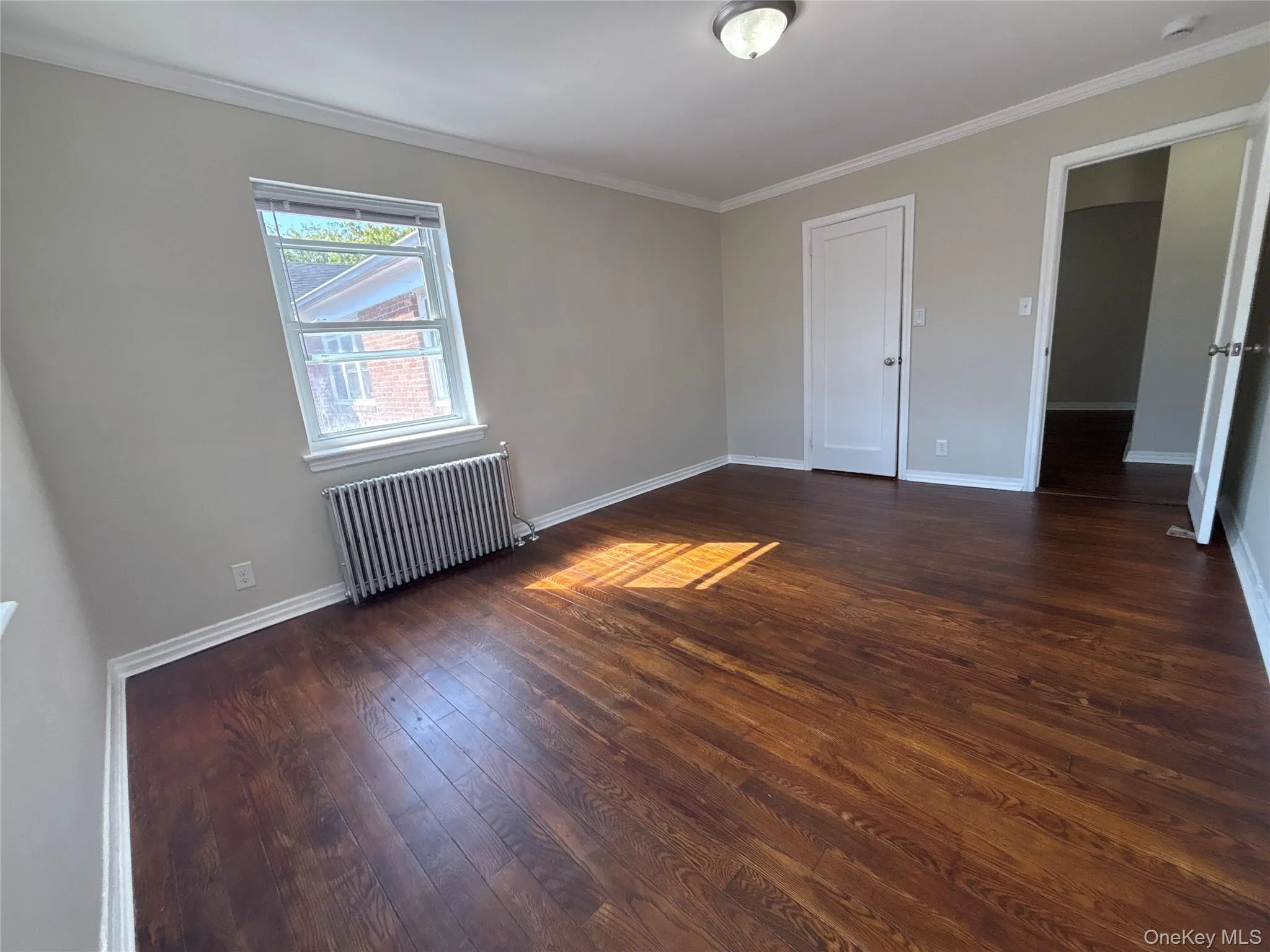 Unfurnished bedroom with crown molding, radiator, and dark wood-style floors Unfurnished bedroom with crown molding, radiator, and dark wood-style floors