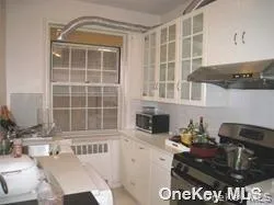 Kitchen with white cabinets, stainless steel appliances, light countertops, exhaust hood, and radiator Kitchen with white cabinets, stainless steel appliances, light countertops, exhaust hood, and radiator